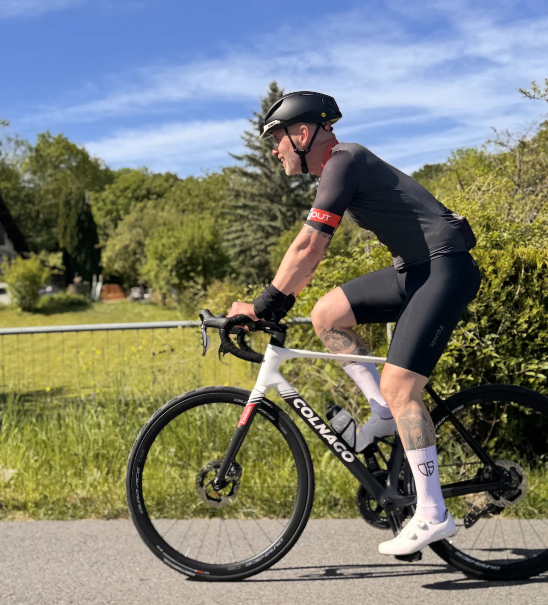 Cycliste en tenue noire roulant sur un vélo Colnago le long d'une route de campagne
